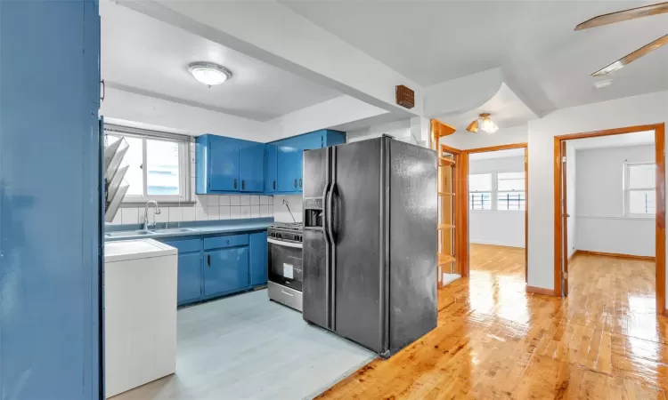 Kitchen with sink, stainless steel range with gas cooktop, black refrigerator with ice dispenser, blue cabinets, and decorative backsplash