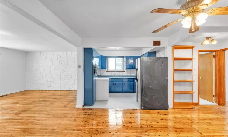 Kitchen featuring black refrigerator, sink, blue cabinetry, tasteful backsplash, and light hardwood / wood-style floors