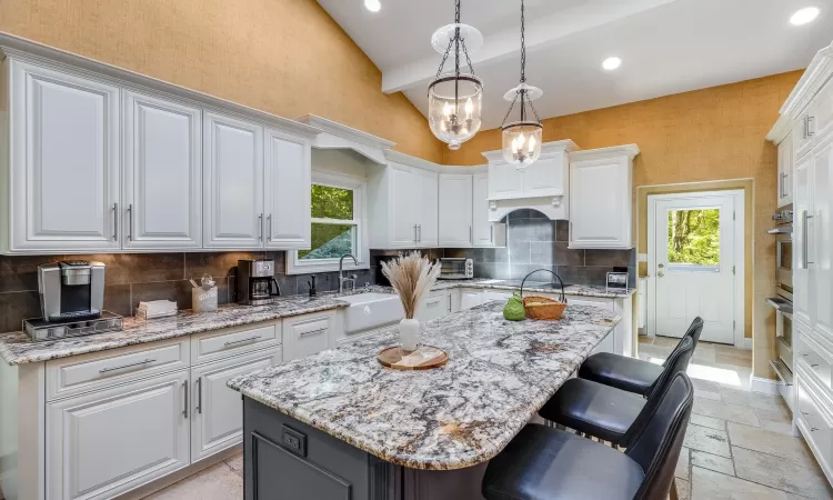 Kitchen with white cabinetry, hanging light fixtures, light stone counters, backsplash, and a kitchen island