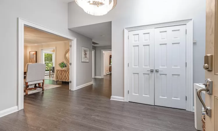 Entrance foyer with ornamental molding, dark wood-type flooring, and an inviting chandelier