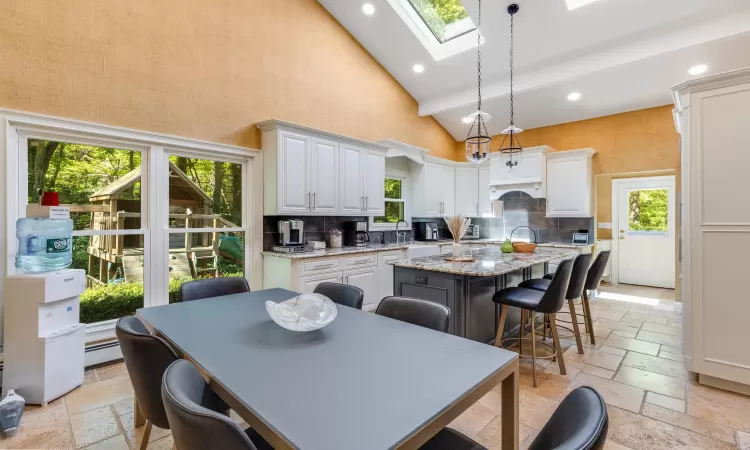 Kitchen featuring a center island, a kitchen breakfast bar, light stone counters, high vaulted ceiling, and pendant lighting