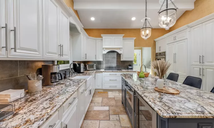 Kitchen with white cabinets, a kitchen island, light stone countertops, and hanging light fixtures