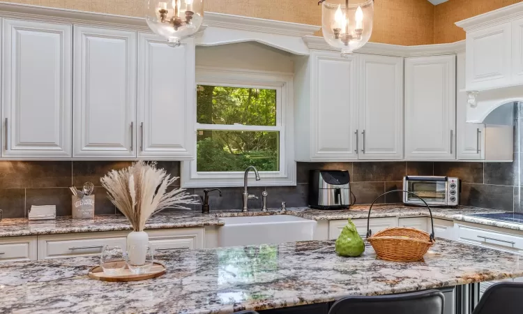 Kitchen featuring light stone countertops, sink, pendant lighting, stovetop, and white cabinetry