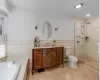 Full bathroom featuring vanity, separate shower and tub, a baseboard heating unit, tile walls, and toilet