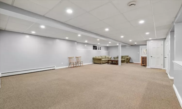 Basement featuring baseboard heating and light carpet