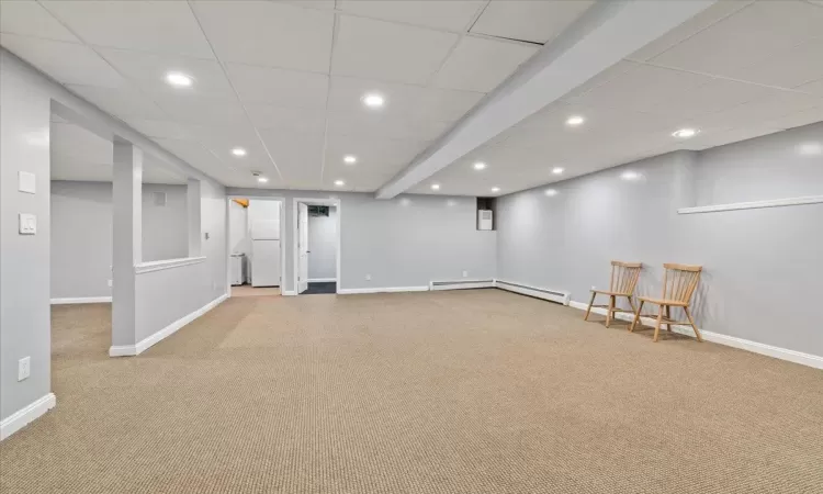 Basement featuring light carpet, a baseboard radiator, and white refrigerator