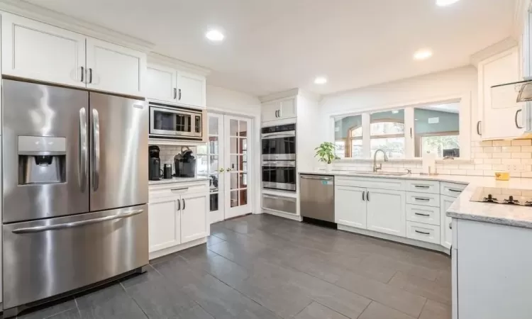 Kitchen featuring decorative backsplash, appliances with stainless steel finishes, white cabinetry, and sink