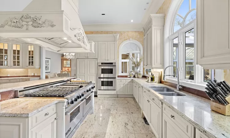 Kitchen featuring white cabinets, sink, light stone counters, custom range hood, and stainless steel appliances