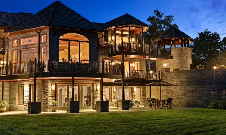 Back house at dusk featuring a lawn, a balcony, and a patio