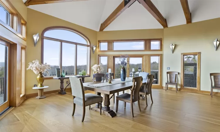 Dining area with beam ceiling, light hardwood / wood-style floors, high vaulted ceiling, and a wealth of natural light