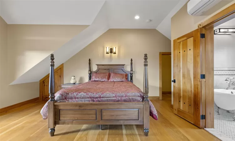 Bedroom with a wall mounted air conditioner, light wood-type flooring, and vaulted ceiling