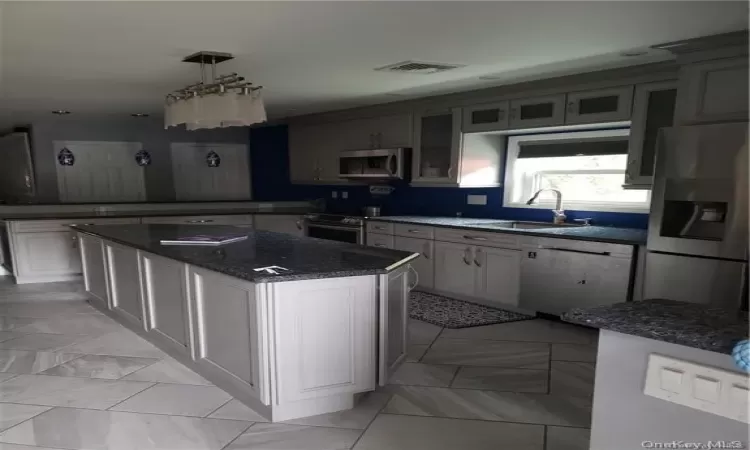 Kitchen with sink, hanging light fixtures, dark stone countertops, a kitchen island, and stainless steel appliances