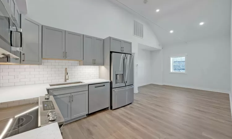 Kitchen with appliances with stainless steel finishes, gray cabinets, light hardwood / wood-style floors, and sink