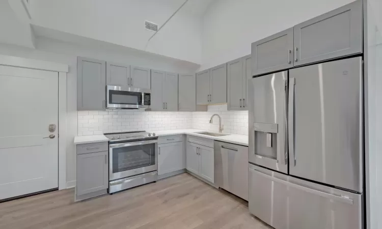 Kitchen with backsplash, stainless steel appliances, sink, light hardwood / wood-style flooring, and gray cabinets