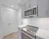 Kitchen featuring decorative backsplash, light stone counters, gray cabinetry, stainless steel appliances, and light hardwood / wood-style floors