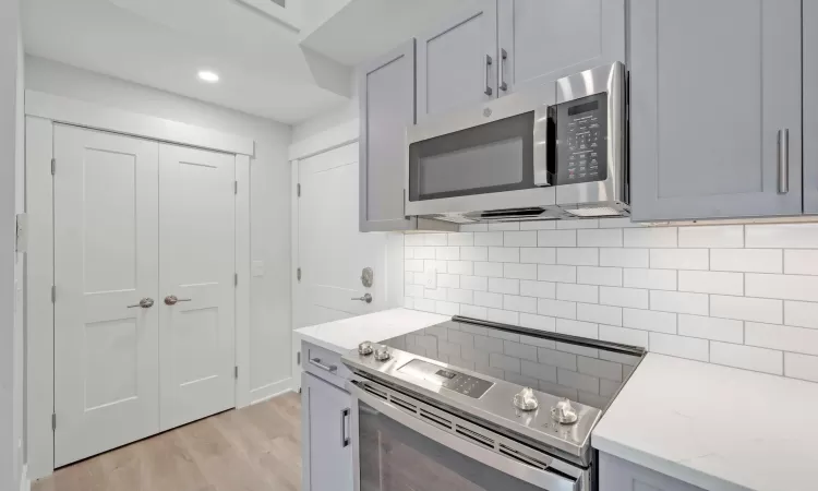 Kitchen featuring decorative backsplash, light stone counters, gray cabinetry, stainless steel appliances, and light hardwood / wood-style floors