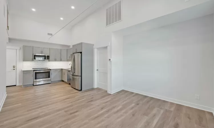 Kitchen featuring a high ceiling, light hardwood / wood-style flooring, gray cabinets, tasteful backsplash, and stainless steel appliances