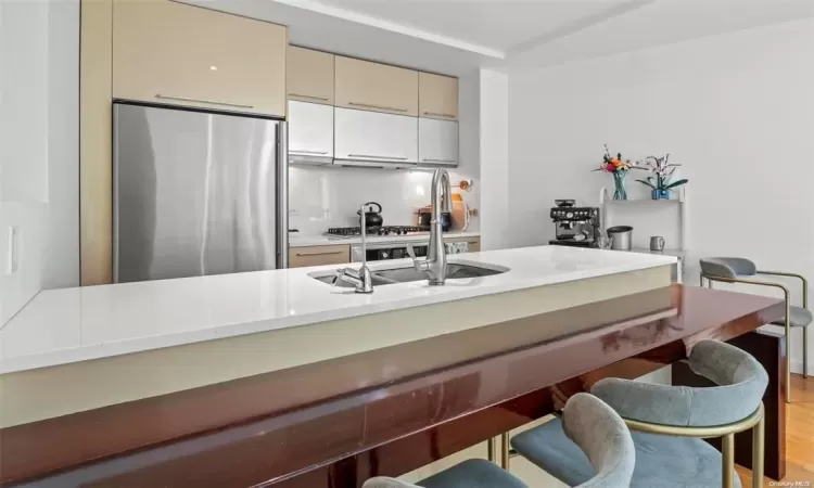 Kitchen with sink, vaulted ceiling, stainless steel fridge, light wood-type flooring, and cream cabinetry