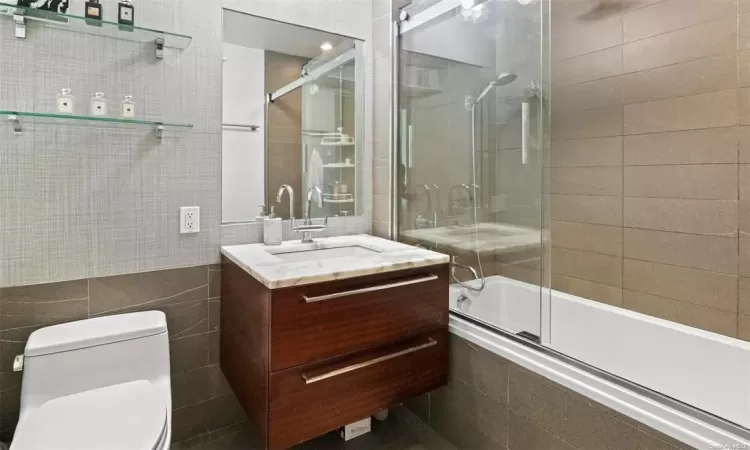 Full bathroom with vanity, toilet, enclosed tub / shower combo, and tile walls