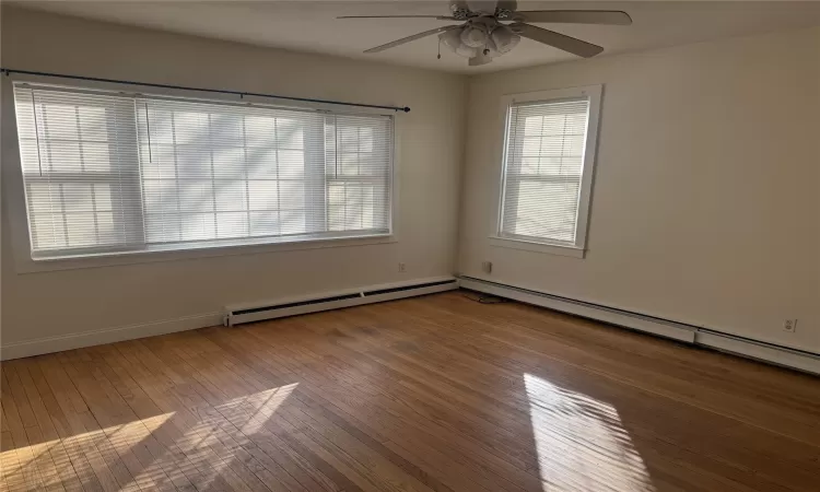 Unfurnished room featuring hardwood / wood-style floors, ceiling fan, and a baseboard radiator