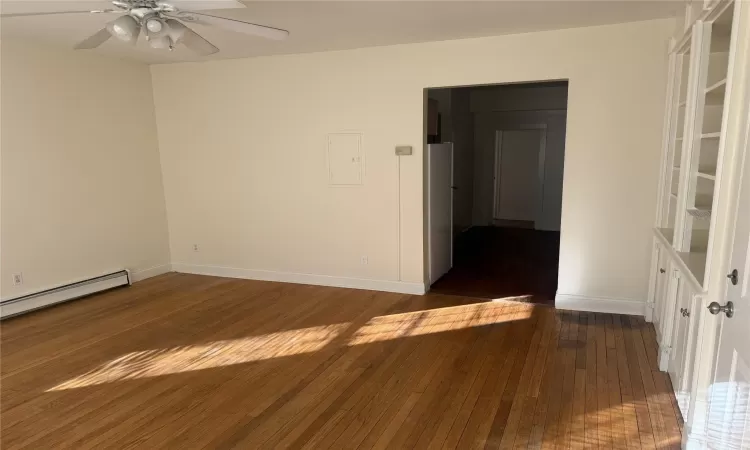 Empty room featuring ceiling fan, dark wood-type flooring, and a baseboard heating unit