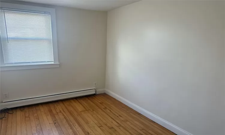 Unfurnished room featuring a healthy amount of sunlight, light wood-type flooring, and a baseboard heating unit