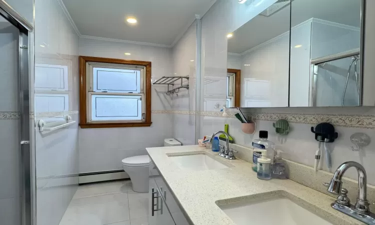 Bathroom featuring baseboard heating, vanity, tile walls, and ornamental molding