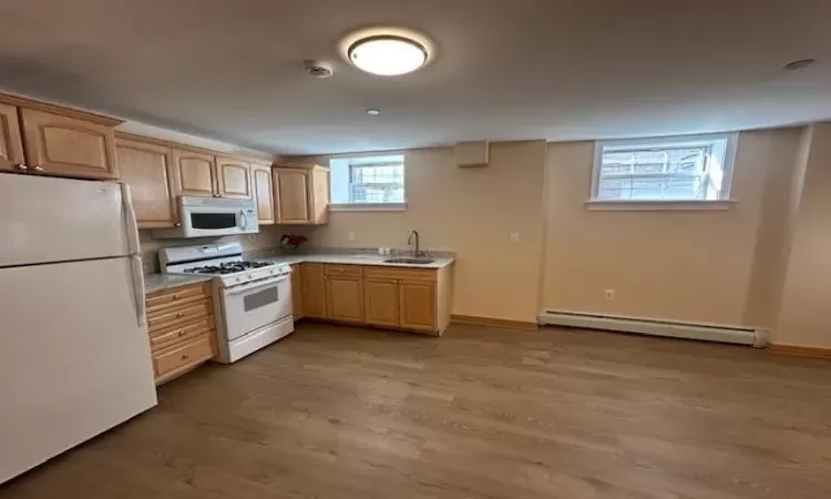 Kitchen with hardwood / wood-style floors, white appliances, sink, light brown cabinetry, and a baseboard radiator