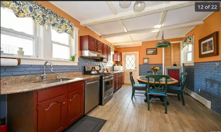 Kitchen featuring sink, baseboard heating, appliances with stainless steel finishes, light hardwood / wood-style floors, and brick wall