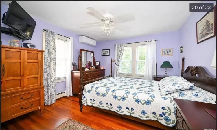 Bedroom featuring multiple windows, dark hardwood / wood-style floors, a wall unit AC, and ceiling fan