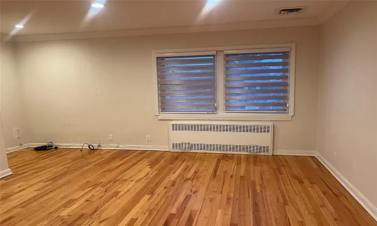 Empty room with crown molding, radiator heating unit, and light wood-type flooring