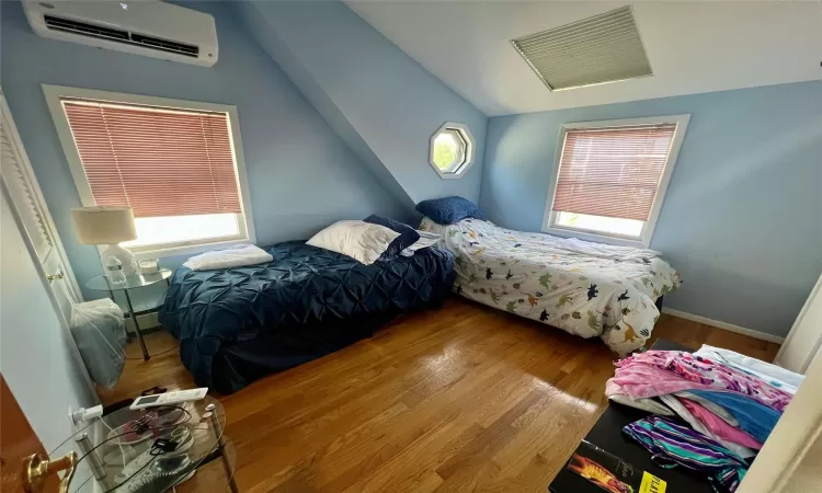 Bedroom with hardwood / wood-style flooring, an AC wall unit, baseboard heating, and lofted ceiling