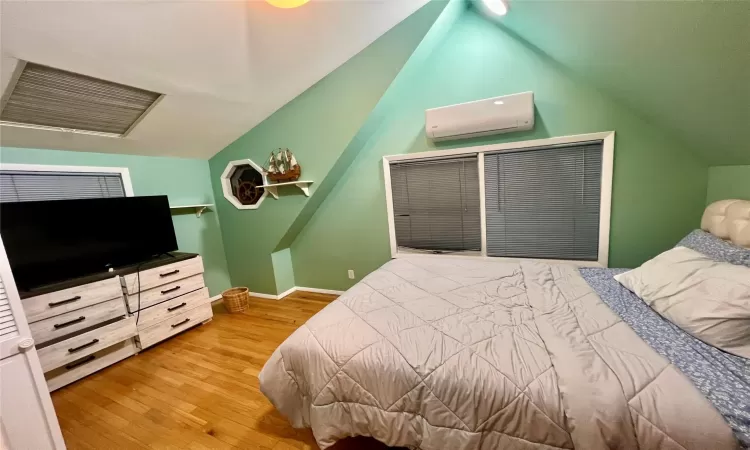 Bedroom with vaulted ceiling, wood-type flooring, and a wall mounted air conditioner