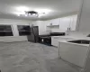 Kitchen featuring white cabinetry, sink, black gas range oven, a notable chandelier, and stainless steel fridge