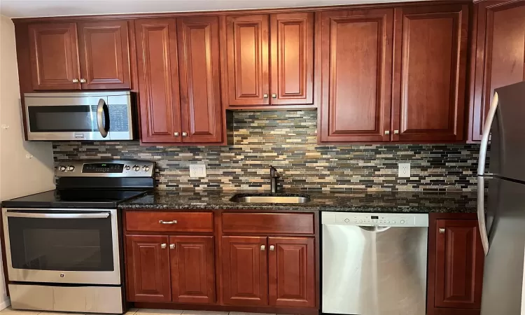 Kitchen with backsplash, dark stone countertops, sink, and appliances with stainless steel finishes