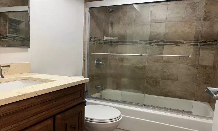 Full bathroom featuring shower / bath combination with glass door, vanity, and toilet