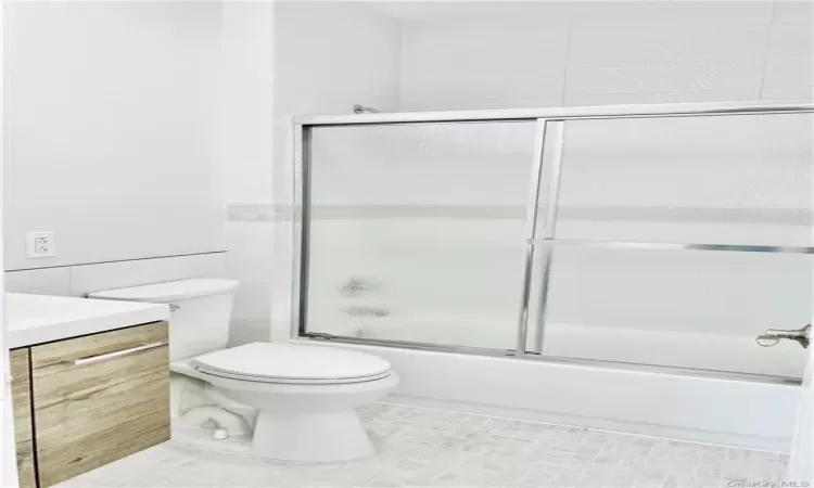 Full bathroom with shower / bath combination with glass door, tile patterned floors, vanity, and toilet