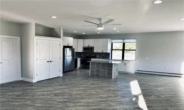 Kitchen featuring a kitchen island, white cabinets, a baseboard heating unit, and appliances with stainless steel finishes