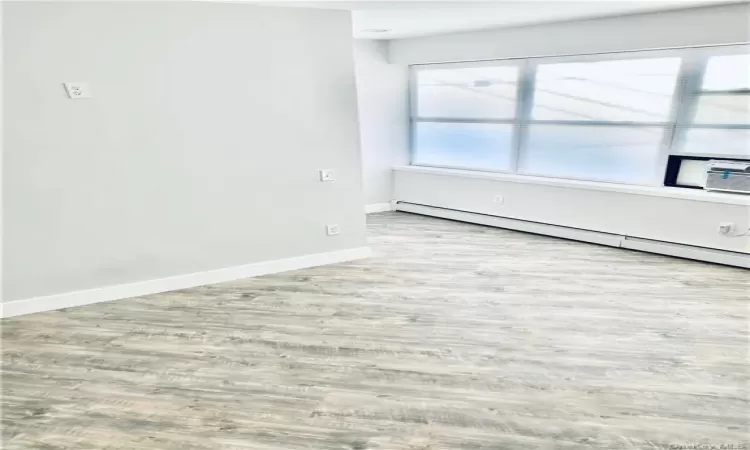 Empty room featuring light wood-type flooring, a baseboard radiator, and cooling unit