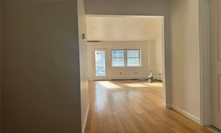 Corridor with light hardwood / wood-style floors, baseboard heating, and a wall unit AC