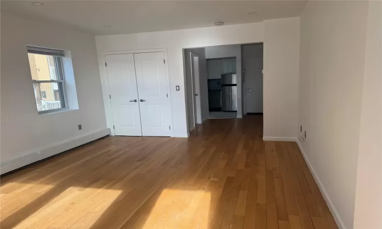 Unfurnished bedroom featuring hardwood / wood-style floors, stainless steel refrigerator, and baseboard heating