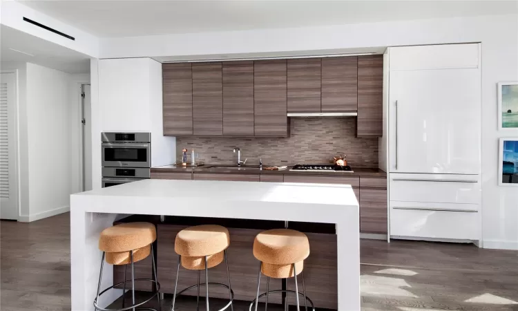 Kitchen with a kitchen breakfast bar, sink, decorative backsplash, dark hardwood / wood-style floors, and appliances with stainless steel finishes