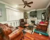 Living room with ceiling fan, baseboard heating, a stone fireplace, hardwood / wood-style floors, and ornamental molding