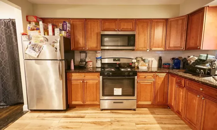 Kitchen featuring light wood-type flooring, stainless steel appliances, tasteful backsplash, and dark stone counters