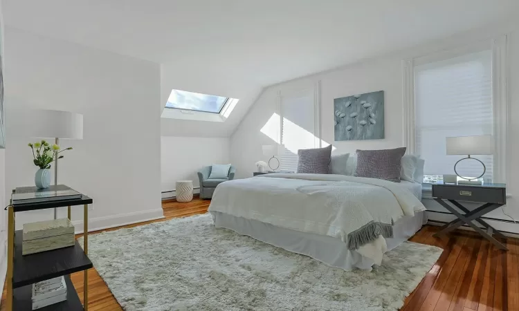 Primary Bedroom featuring hardwood  floors, lofted ceiling with skylight & walk-in closet