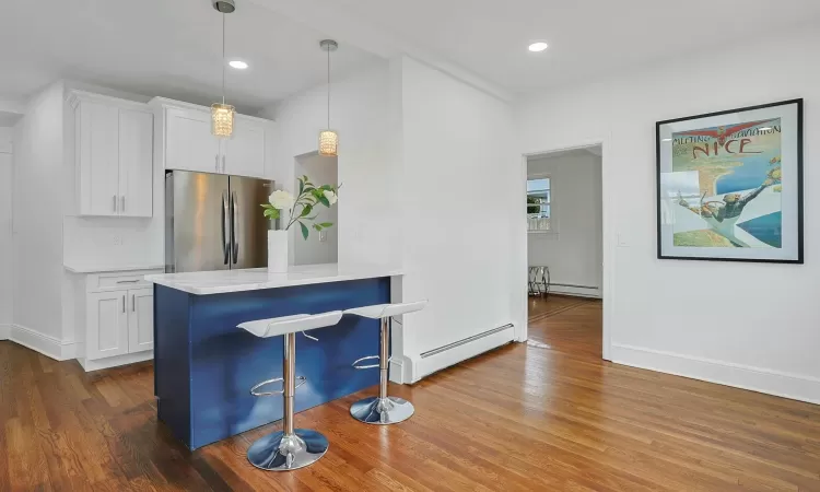 Kitchen featuring white cabinetry, hanging light fixtures, stainless steel refrigerator, and a baseboard heating unit