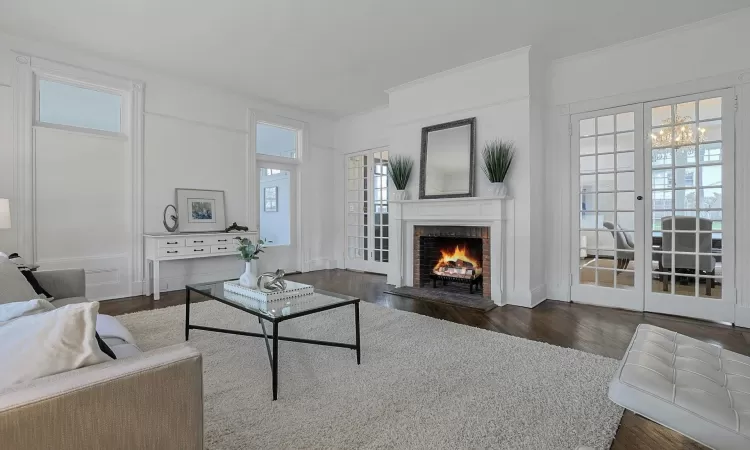 Living room with a brick fireplace, ornamental molding, dark wood-type flooring, and french doors