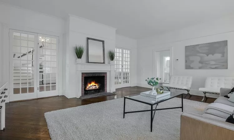 Living room featuring dark wood-type flooring, an inviting chandelier, french doors, ornamental molding, and a fireplace