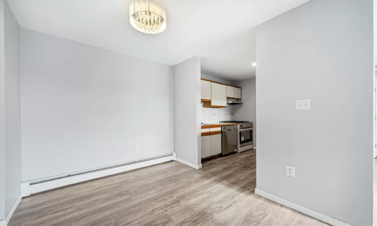 Kitchen with white cabinetry, a baseboard heating unit, light hardwood / wood-style floors, decorative backsplash, and appliances with stainless steel finishes