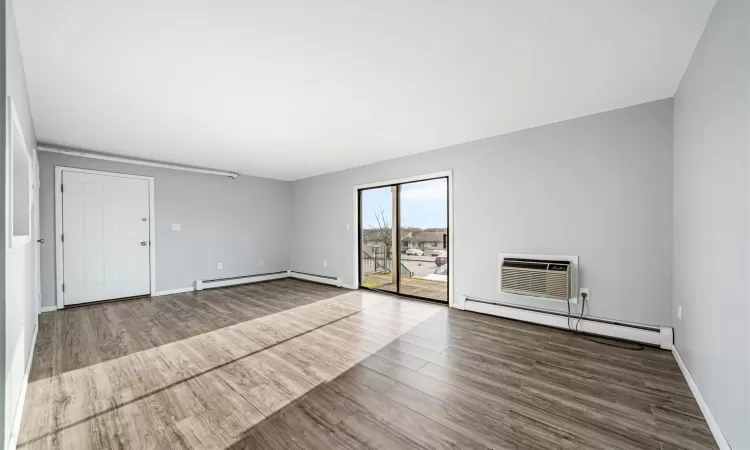 Unfurnished room with wood-type flooring, a wall unit AC, and a baseboard heating unit